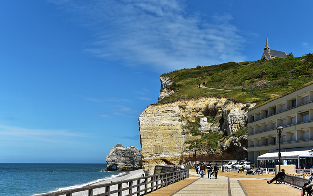 Promenade am Meer mit Klippen und einer kleinen Kirche im Hintergrund.