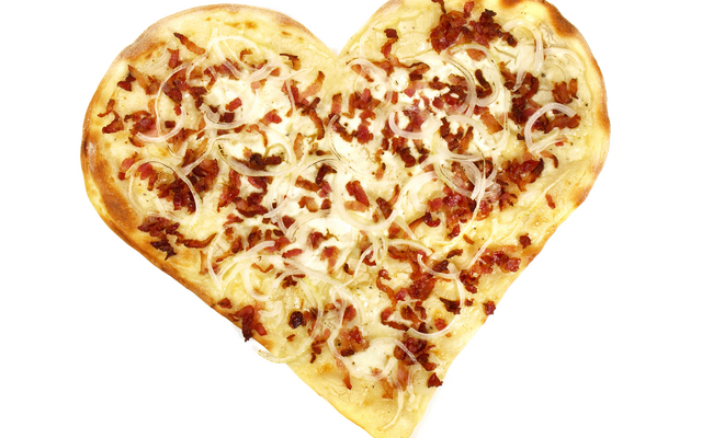Ein herzförmiger Flammkuchen mit Speck und Zwiebeln auf weißem Hintergrund.