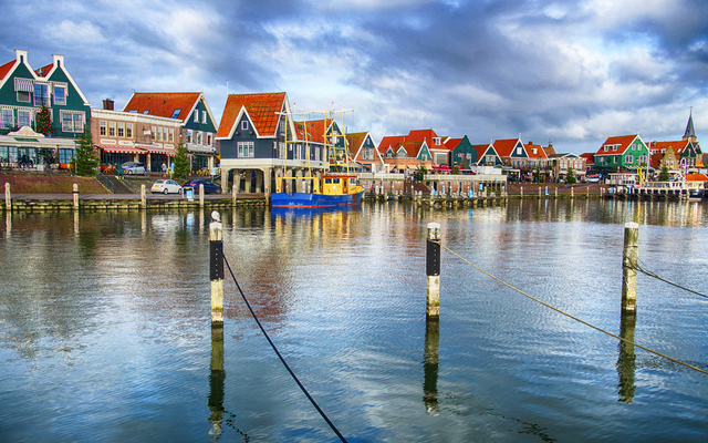 Hafen mit bunten Häusern und Boot, unter bewölktem Himmel.