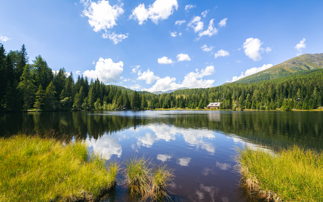 See mit Wald und Bergen im Hintergrund unter blauem Himmel mit Wolken.