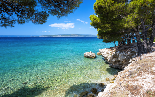 Küstenlandschaft mit klarem blauem Meer und Felsen, umgeben von Pinien.