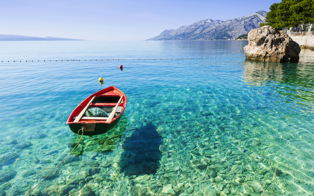 Rotes Boot auf klarem, türkisfarbenem Wasser vor einer felsigen Küste.
