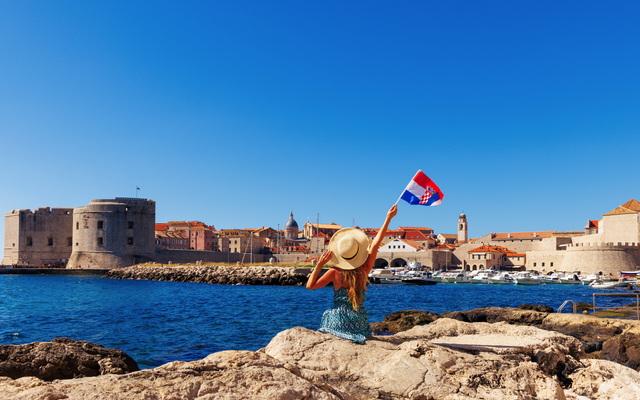 Frau am Meer hält kroatische Flagge vor Altstadt von Dubrovnik.