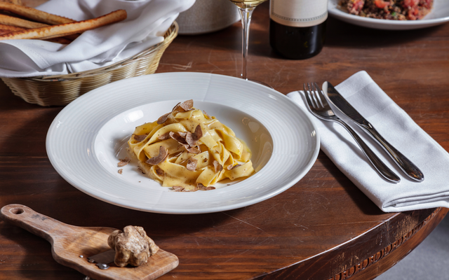 Pasta mit Trüffeln auf einem Holztisch, flankiert von Besteck und einem Brotkorb.