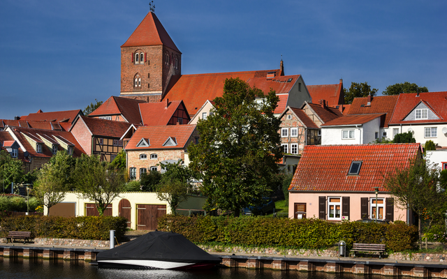 Stadtansicht mit Kirche und Fachwerkhäusern am Wasser.