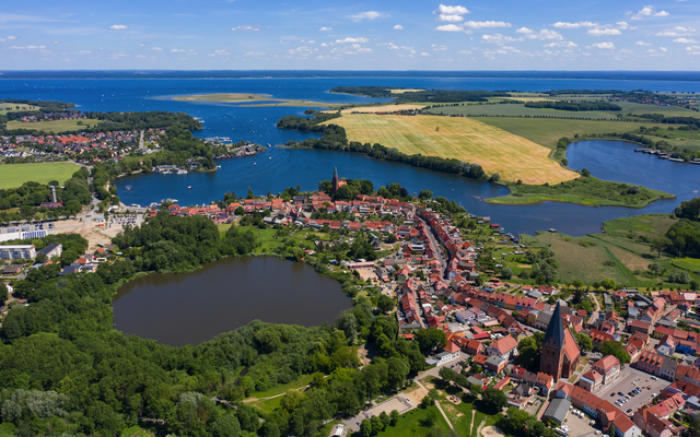 Luftaufnahme einer Stadtlandschaft mit Seen und Feldern im Hintergrund.