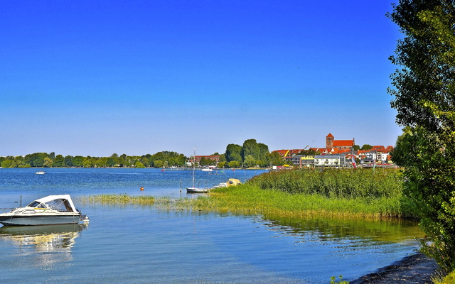 Seeufer mit Boot, grünem Ufer und Stadt im Hintergrund an einem klaren Tag.