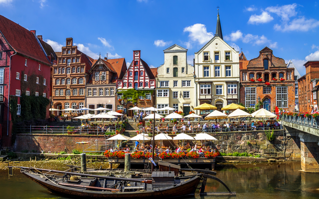 Fachwerkhäuser und ein traditionelles Boot an einem Flussufer bei Sonnenschein.