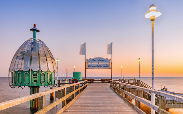 Seebrücke bei Sonnenuntergang mit Tauchgondel und Laternen am Meer.