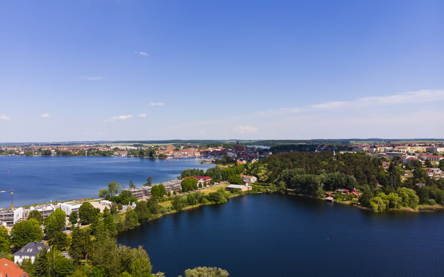 Landschaft mit Seen, grünen Ufern und blauen Himmel im Hintergrund.