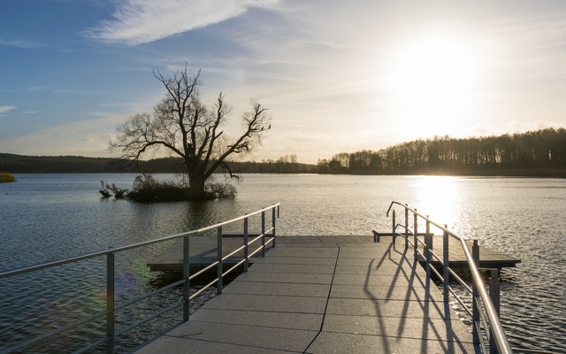 Steg über See mit Sonne und Insel im Hintergrund