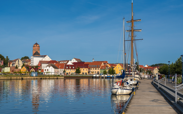 Hafen mit Segelbooten, bunte Gebäude und Kirchturm im Hintergrund.