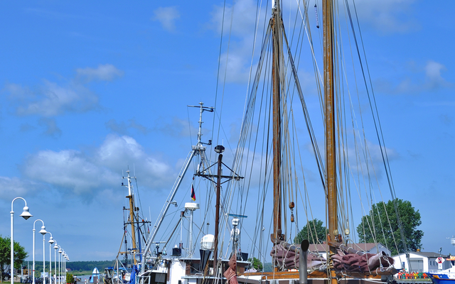 Segelschiffe im Hafen bei blauem Himmel und Wolken.