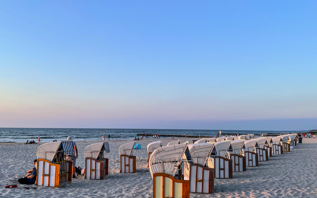 Strandkörbe am Sandstrand bei Sonnenuntergang mit Meer im Hintergrund