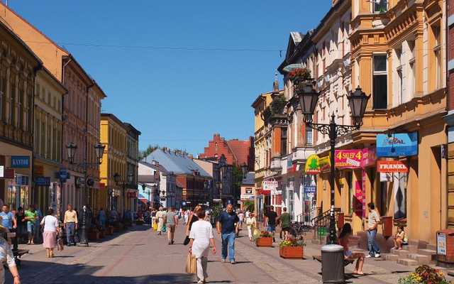 Menschen spazieren durch eine sonnige Fußgängerzone mit historischen Gebäuden.