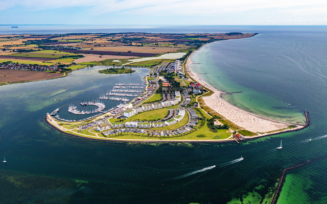 Luftaufnahme einer Küstenlandschaft mit Yachthafen und Sandstrand.