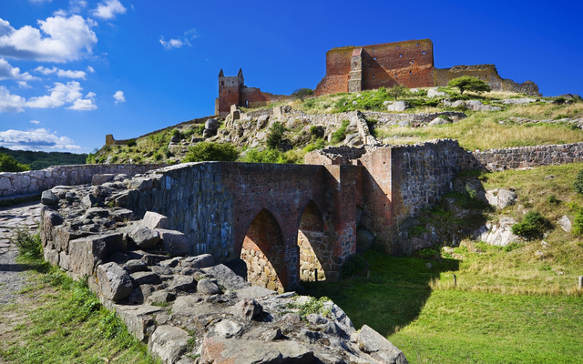 Ruine einer mittelalterlichen Burg auf einem Hügel unter blauem Himmel.