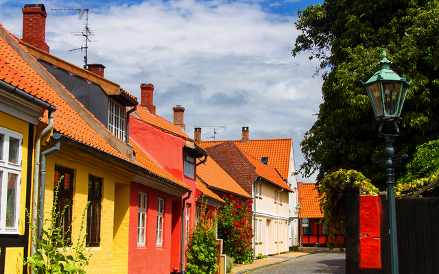 Pflasterstraße mit bunten Häusern und Laterne in einer ruhigen, sonnigen Gasse.