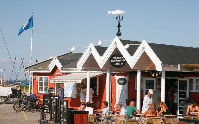 Fischrestaurant mit rotem Gebäude und Gartenmöbeln, Blauer Himmel im Hintergrund.