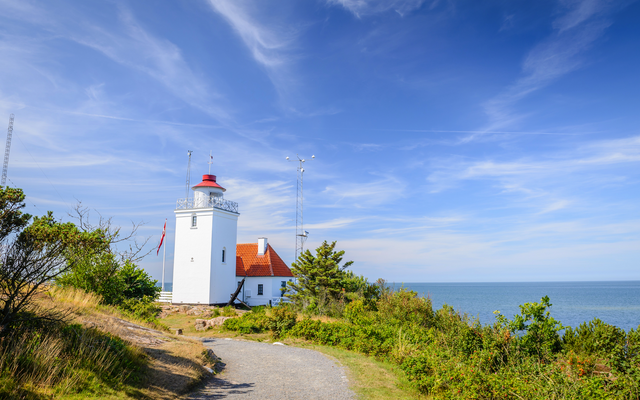 Weißer Leuchtturm auf Klippe mit Meerblick bei blauem Himmel.