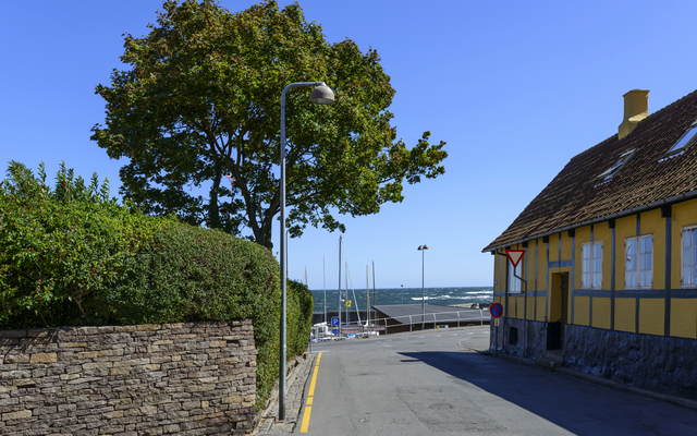 Straßenecke mit gelbem Fachwerkhaus, Baum, Straßenschild und Blick auf das Meer.