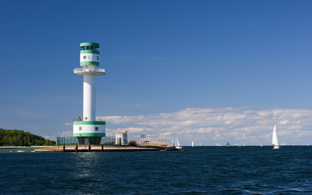 Leuchtturm am Meer mit Segelbooten im Hintergrund bei klarem Himmel