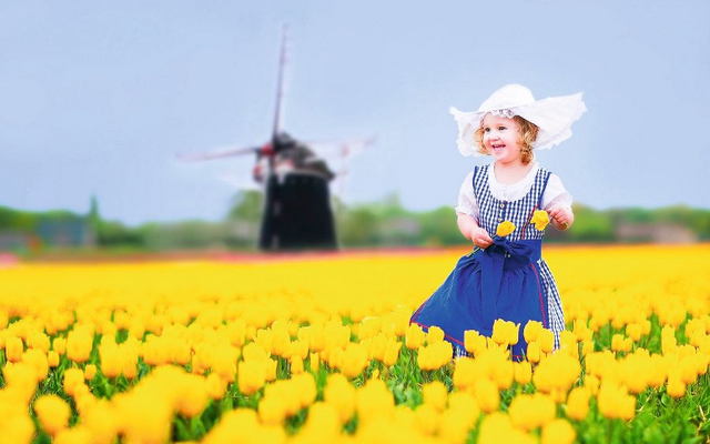 Kind in Tracht mit Tulpenfeld und Windmühle im Hintergrund.