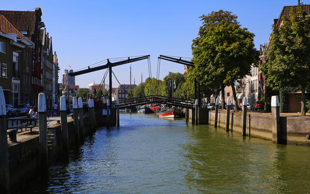 Kanal mit beweglicher Brücke, flankiert von Bäumen und Gebäuden bei klarem Himmel.