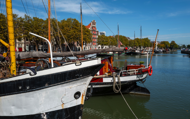 Boote am Ufer eines Kanals mit Stadtansicht im Hintergrund.
