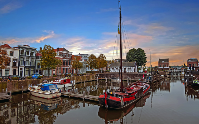 Hafen mit traditionellen Booten und historischen Gebäuden im Hintergrund bei Sonnenuntergang.