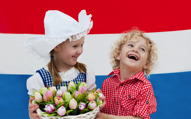 Ein Mädchen und ein Junge mit Tulpen vor einer niederländischen Flagge.