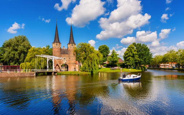 Kirche mit Türmen am Wasser, Boot auf dem Fluss, blauer Himmel mit Wolken.