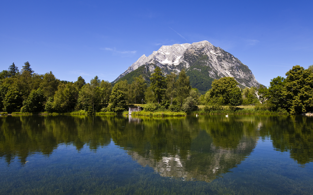 Bergspiegelung in einem klaren See unter blauem Himmel.