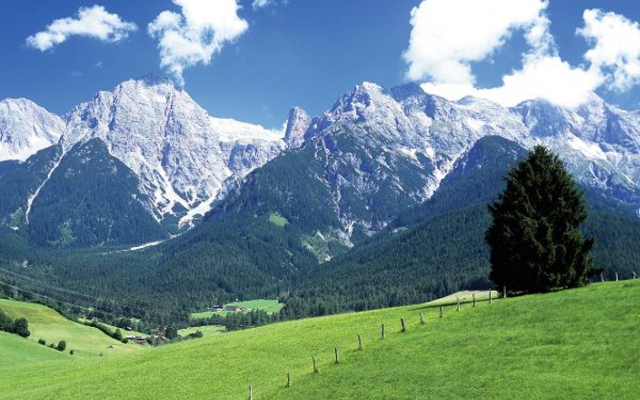Grüne Wiesen vor schneebedeckten Bergen und blauem Himmel mit Wolken.