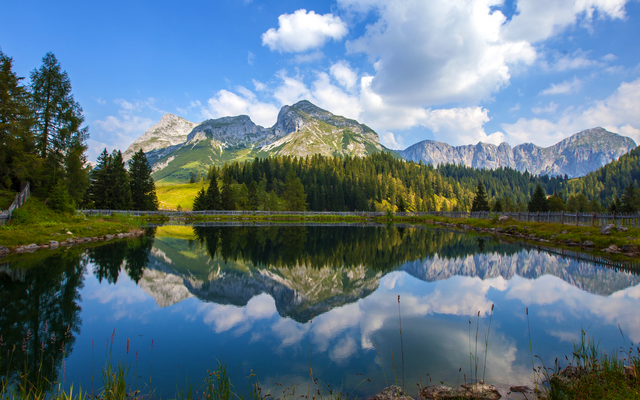 See mit Berglandschaft und Spiegelung im Wasser bei Sonnenschein.