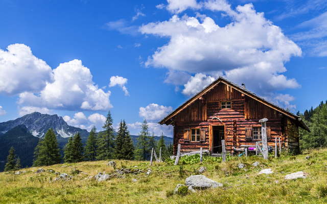 Holzhütte in alpiner Landschaft mit Bergen und blauem Himmel im Hintergrund.