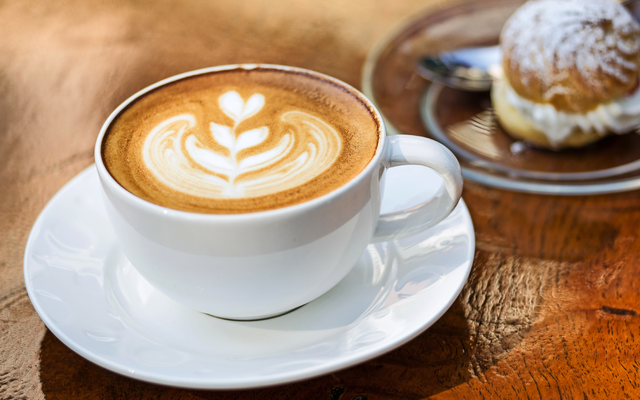 Eine Tasse Cappuccino mit Latte Art neben einem Gebäck.