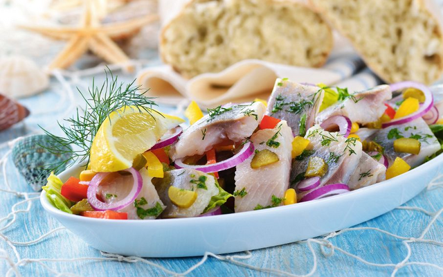 Schüssel mit eingelegtem Hering, Zwiebeln und Zitronenscheiben, im Hintergrund Brot.