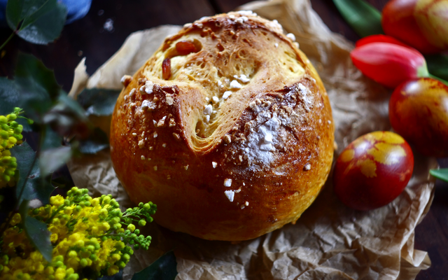 Osterbrot auf Pergamentpapier mit Blumen und bunt bemalten Eiern.