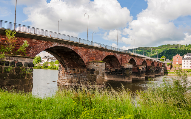 Steinbrücke über einen Fluss mit bewölktem Himmel im Hintergrund.