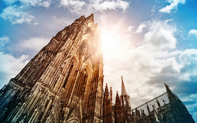 Sonnenschein hinter einer gotischen Kathedrale mit Wolken am Himmel.