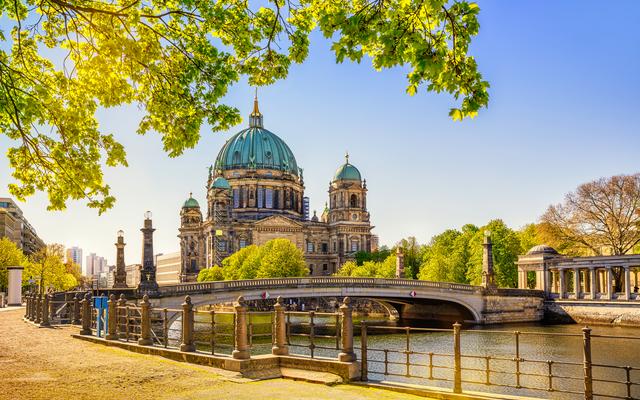 Berliner Dom im Sommer bei sonnigem Wetter, an der Spree gelegen, umgeben von grünen Bäumen.