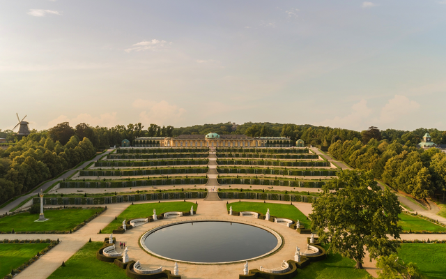 Schloss Sanssouci mit Terrassengärten im Sommer, Blick auf Fontäne und Bäume.