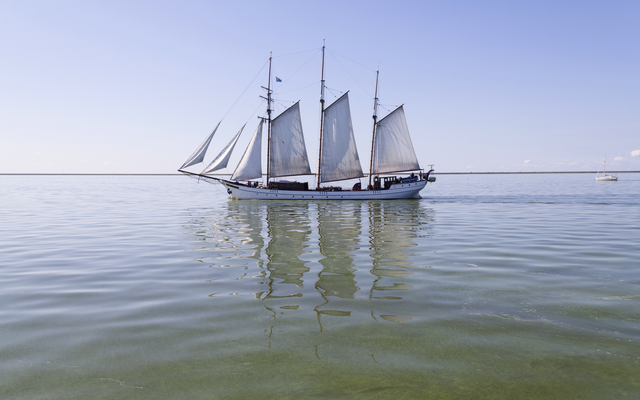 Segelschiff mit vier Masten auf ruhigem Meer unter blauem Himmel.