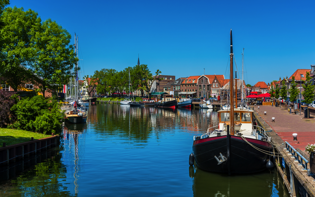 Boote in einem ruhigen Kanalufer mit Dorf und blauem Himmel im Hintergrund