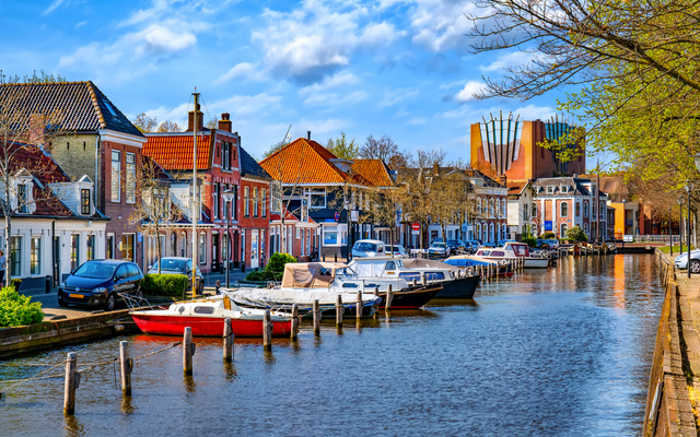 Kanal mit angrenzenden Häusern, Booten und Bäumen unter blauem Himmel.