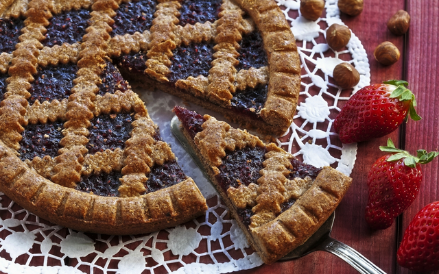 Gedeckte Linzer Torte auf Spitzenunterlage mit Erdbeeren und Haselnüssen