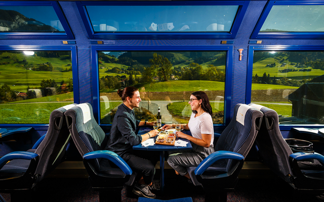 Zwei Personen essen in einem Zug mit Panoramafenstern.