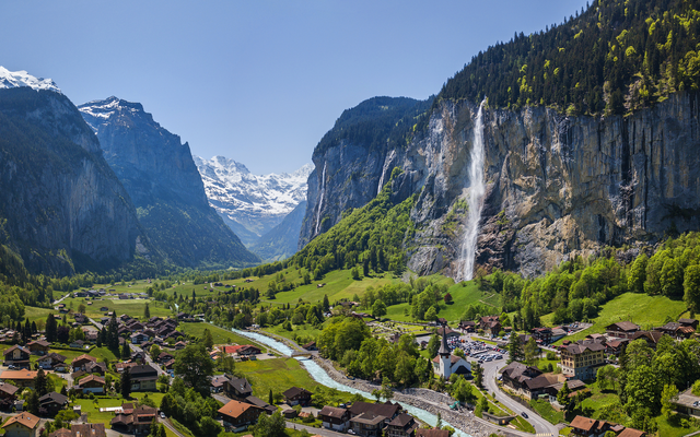 Landschaft mit Dorf, Fluss, Wasserfall und schneebedeckten Bergen im Hintergrund
