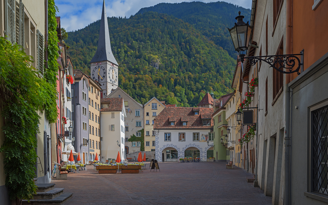 Malerische Altstadtgasse mit Kirchturm und Bergen im Hintergrund.